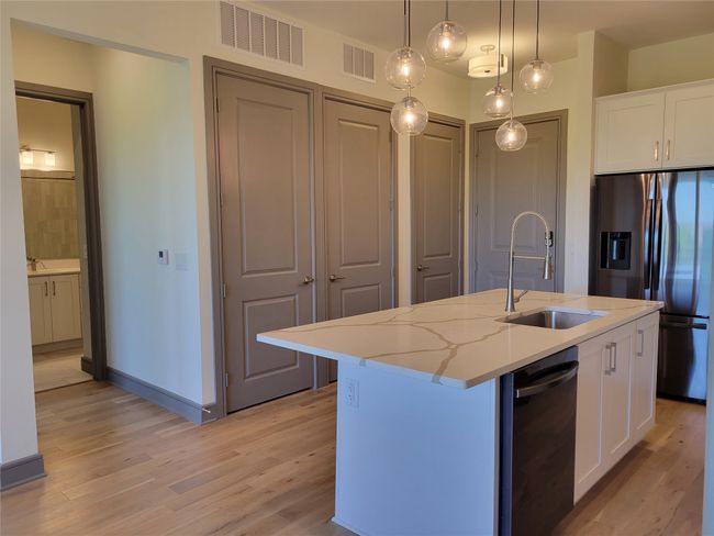 Kitchen featuring a sink, stainless steel fridge with ice dispenser, light wood finished floors, and white cabinetry | Image 8