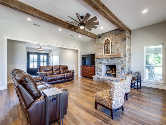 Grand living area. Incredible barn wood beams, massive stone fireplace with large rustic mantle. Hearth creates extra seating as needed. Lots of windows give you beautiful 360 views and lots of natural sunlight. Notice the rich warm wood-look floors. Carefully chosen fan is the perfect accent. | Image 5