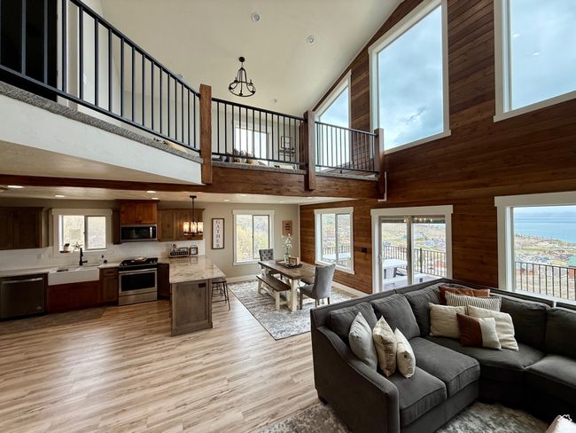 Living room with plenty of natural light, a towering ceiling, light wood-type flooring, wooden walls, and an inviting chandelier | Image 14