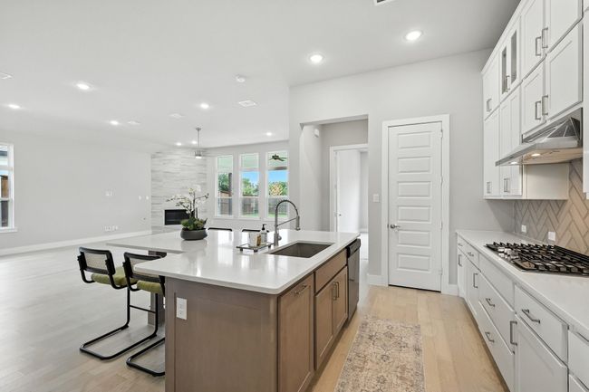 Kitchen with appliances with stainless steel finishes, under cabinet range hood, light wood-style floors, backsplash, and a kitchen island with sink | Image 6