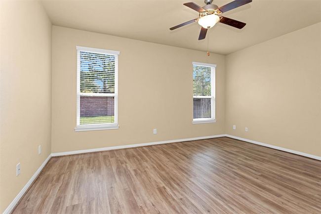 The primary retreat boasts a high ceiling, a stylish ceiling fan, and durable luxury vinyl plank flooring. Large windows invite soft natural light to fill the room, enhancing its warmth and comfort. Walls painted in a serene, neutral tone provide a calming backdrop. | Image 12