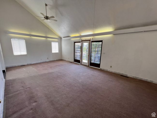 Carpeted empty room featuring ceiling fan, high vaulted ceiling, and baseboards | Image 8