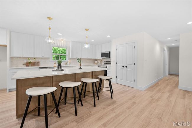 Kitchen featuring stainless steel appliances, light wood finished floors, white cabinetry, a kitchen island, and recessed lighting | Image 14