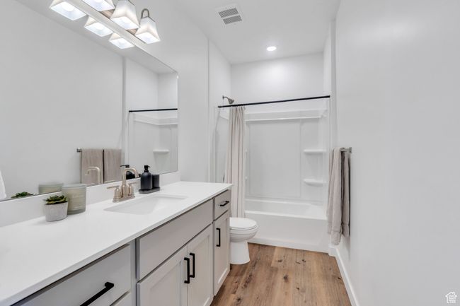 Full bathroom featuring shower / bath combination with curtain, vanity, visible vents, toilet, and wood finished floors | Image 10