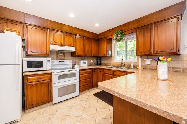 Kitchen with a sink, brown cabinets, under cabinet range hood, and white appliances | Image 16