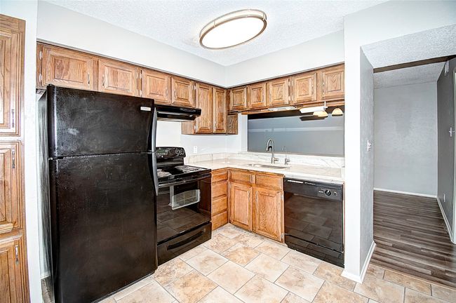 Kitchen featuring sink, a textured ceiling, light tile patterned floors, and black appliances | Image 17