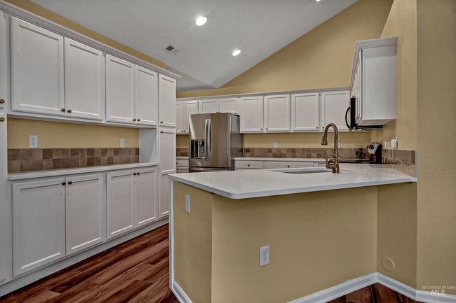 Kitchen featuring stainless steel refrigerator with ice dispenser, a peninsula, decorative backsplash, vaulted ceiling, and dark wood-style flooring | Image 12
