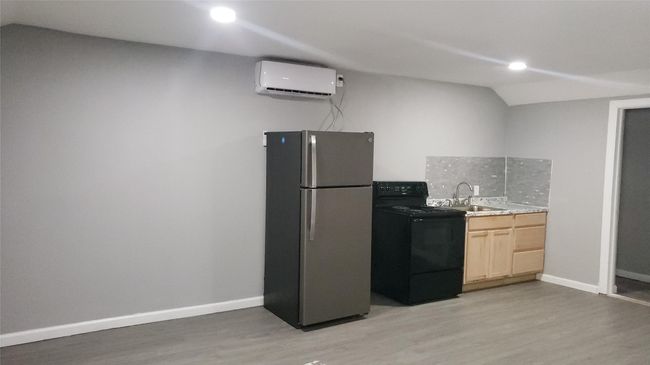 Kitchen featuring black electric range oven, sink, stainless steel fridge, light brown cabinetry, and a wall mounted AC | Image 4