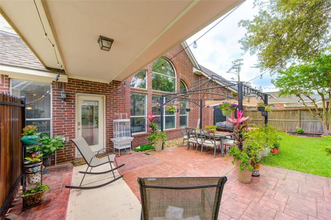 Charming backyard with a covered patio, perfect for outdoor dining and relaxation. Features a brick exterior, lush greenery, and ample space for gardening or entertaining. | Image 8