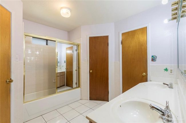 Bathroom with double vanity, tile patterned floors, enclosed tub / shower combo, and tile walls | Image 13