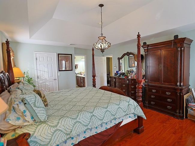 Bedroom featuring visible vents, a tray ceiling, wood finished floors, and ensuite bath | Image 24