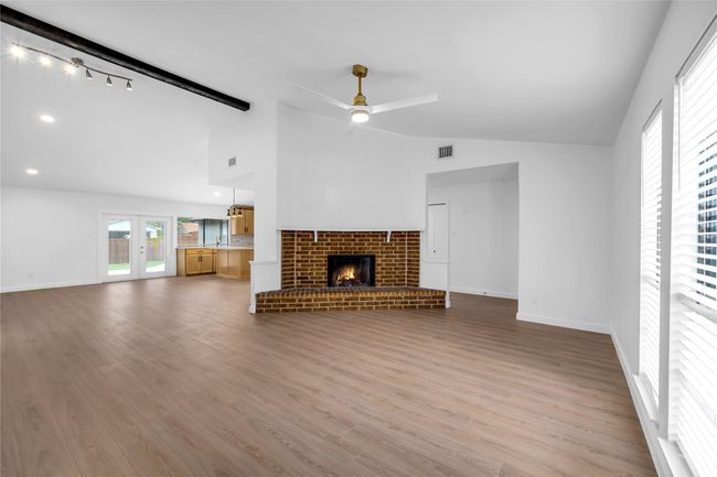 Unfurnished living room featuring ceiling fan, wood finished floors, a brick fireplace, baseboards, and french doors | Image 7