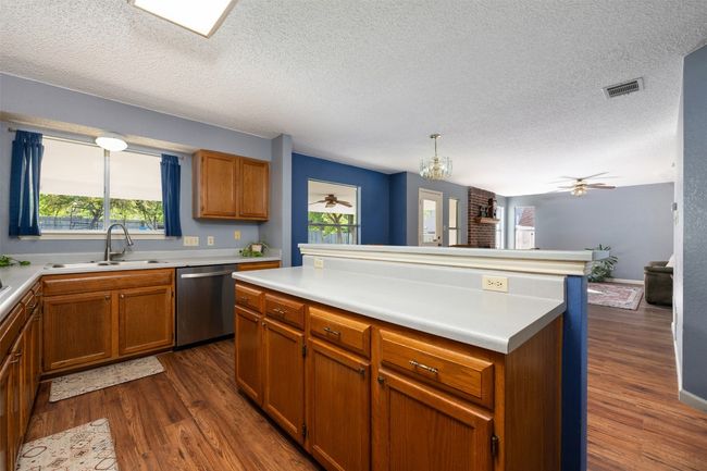 Kitchen with a textured ceiling, visible vents, dark wood finished floors, dishwasher, and a sink | Image 9