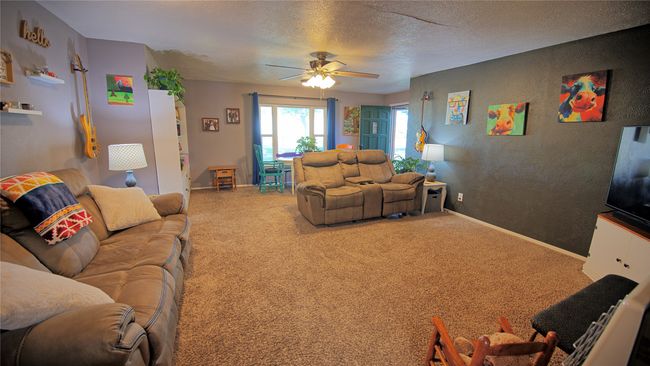 Carpeted living area featuring baseboards, a ceiling fan, a textured wall, and a textured ceiling | Image 4