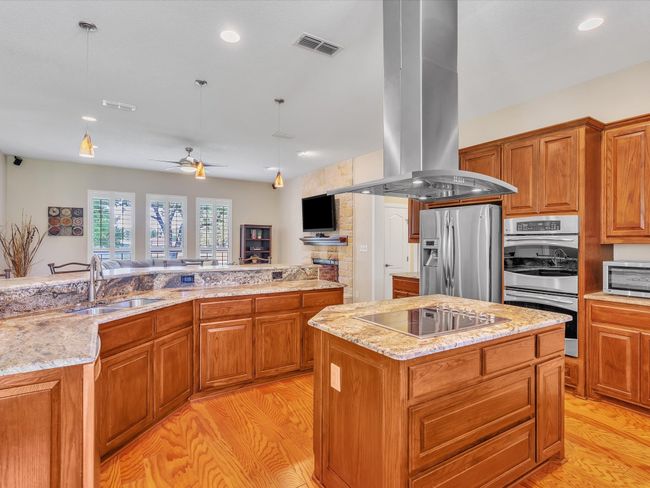 Kitchen with island exhaust hood, stainless steel appliances, a sink, a center island, and light wood-style flooring | Image 11