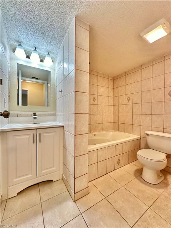 Bathroom with tile walls, tile patterned flooring, tiled tub, a textured ceiling, and vanity | Image 12