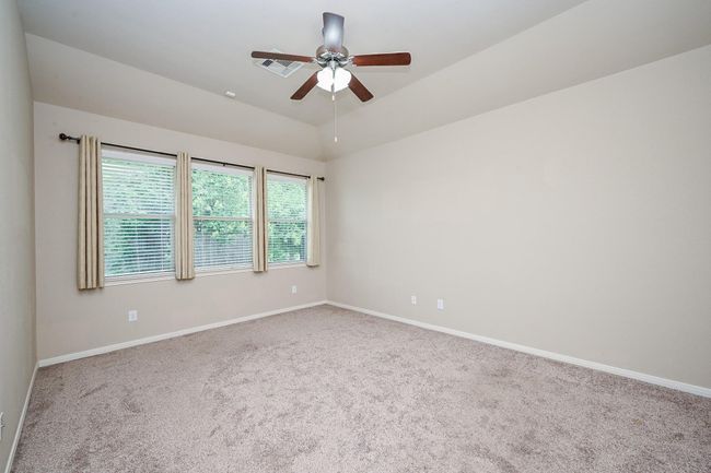 A spacious, carpeted primary bedroom featuring neutral walls, a ceiling fan, and large windows with blinds, offering plenty of natural light. | Image 24