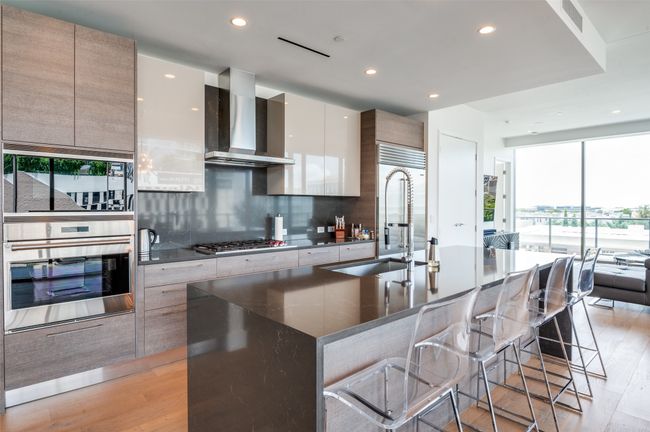 Kitchen with modern cabinets, dark countertops, light wood-style floors, wall chimney exhaust hood, and recessed lighting | Image 10