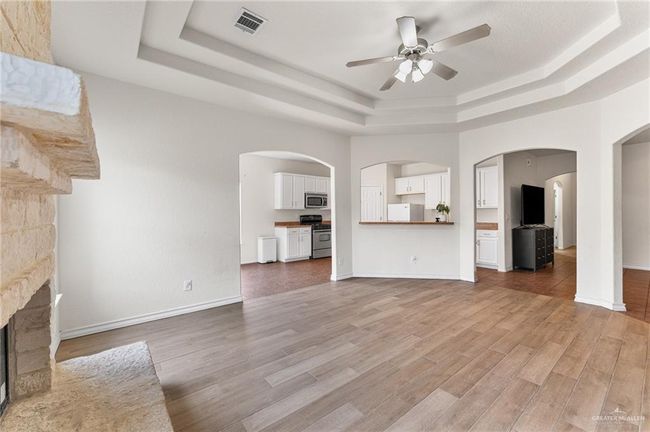 Unfurnished living room with a tray ceiling, a ceiling fan, light wood-type flooring, and a fireplace | Image 14