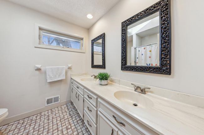 Well-appointed full bathroom featuring a dual-sink vanity, decorative framed mirrors, updated fixtures, and a shower/tub combo with tile flooring. | Image 21