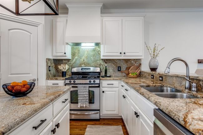 Kitchen featuring stainless steel appliances, custom exhaust hood, white cabinets, crown molding, and dark wood finished floors | Image 11
