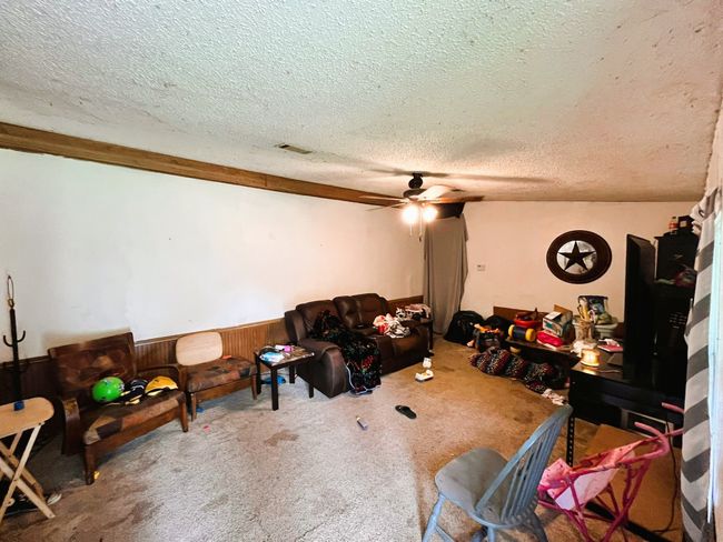 Living area with a textured ceiling, a wainscoted wall, ceiling fan, carpet, and wooden walls | Image 6