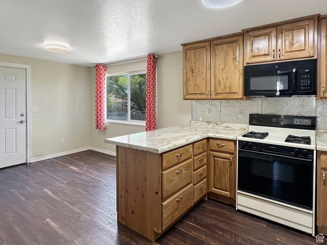 Kitchen with gas stove, black microwave, a peninsula, dark wood-style floors, and decorative backsplash | Image 7