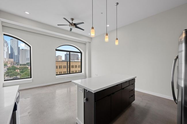 Kitchen with ceiling fan, finished concrete flooring, dark cabinets, freestanding refrigerator, and a kitchen island | Image 4