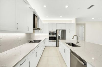 Kitchen featuring light stone counters, sink, wall chimney range hood, white cabinetry, and stainless steel appliances | Image 2