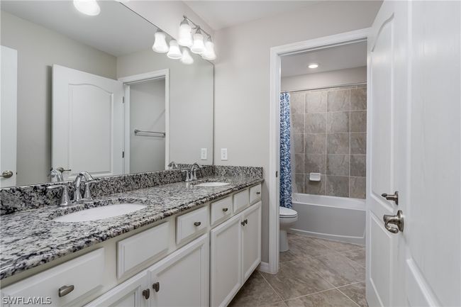 Full bathroom featuring shower / tub combo, double sink, tile floors, large vanity, and toilet | Image 20