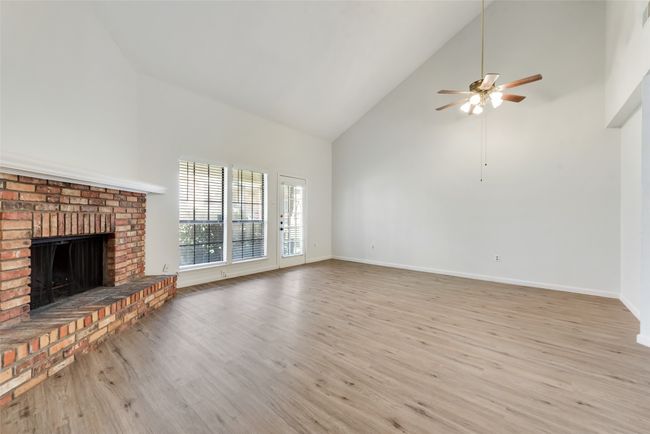 Unfurnished living room with a fireplace, wood finished floors, a ceiling fan, and high vaulted ceiling | Image 7