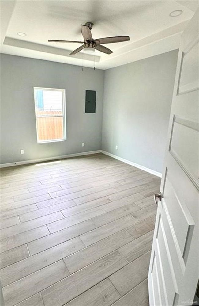 Spare room featuring ceiling fan, baseboards, light wood finished floors, electric panel, and a tray ceiling | Image 9