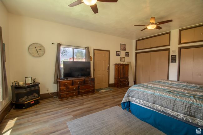 Bedroom with a wood stove, wood finished floors, a ceiling fan, and two closets | Image 15
