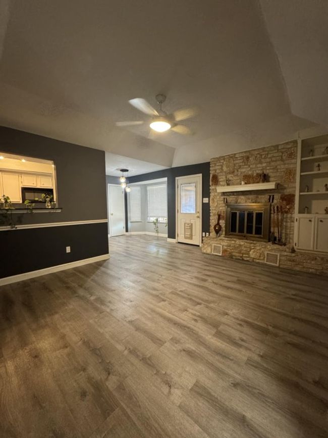 Unfurnished living room featuring wood finished floors, a ceiling fan, a stone fireplace, built in shelves, and vaulted ceiling | Image 5