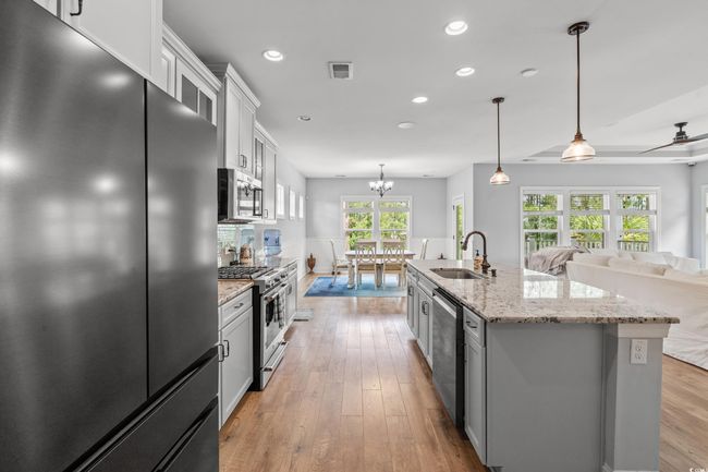 Kitchen with stainless steel appliances, recessed lighting, white cabinets, light wood-type flooring, and a kitchen island with sink | Image 7