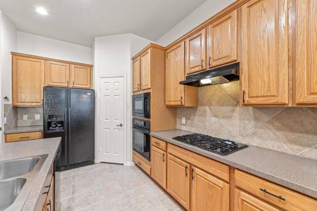 Kitchen with black appliances, under cabinet range hood, tasteful backsplash, light tile patterned floors, and a sink | Image 18