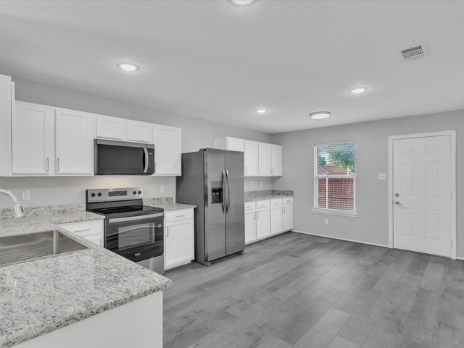 Kitchen featuring stainless steel appliances, a sink, white cabinetry, light wood-type flooring, and light stone counters | Image 24