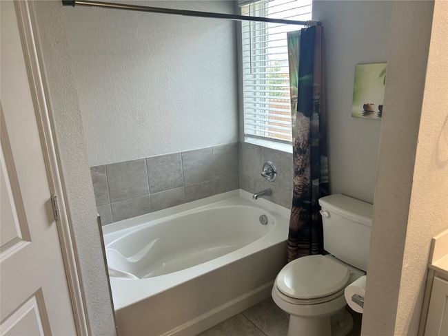 Bathroom with a garden tub, toilet, a textured wall, and tile patterned flooring | Image 9
