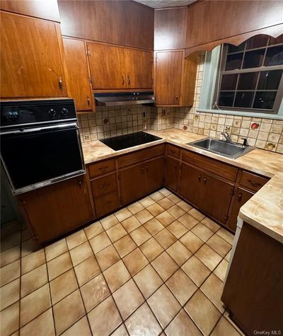 Kitchen featuring black appliances, backsplash, sink, and light tile patterned floors | Image 3