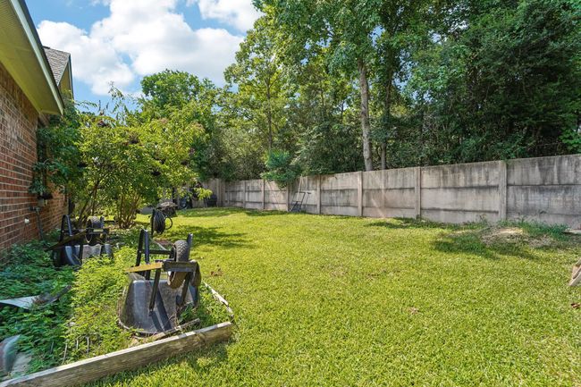 The photo shows a spacious backyard with a well-maintained lawn, bordered by a brick house and a tall concrete fence. There's lush greenery and trees providing privacy and shade. | Image 26