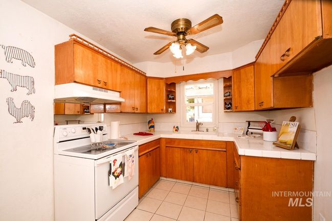 Kitchen with white electric range oven, under cabinet range hood, open shelves, and brown cabinets | Image 9