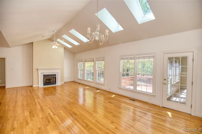 Unfurnished living room with high vaulted ceiling, a skylight, a high end fireplace, light wood-type flooring, and baseboards | Image 6