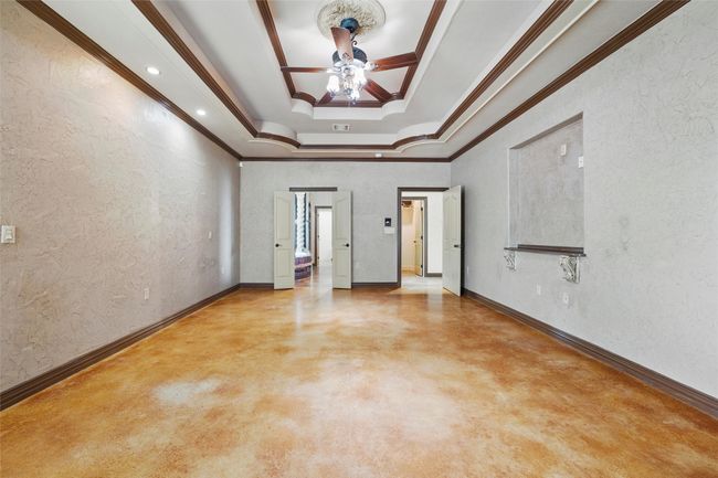 Empty room with a tray ceiling, ceiling fan, concrete floors, ornamental molding, and baseboards | Image 40