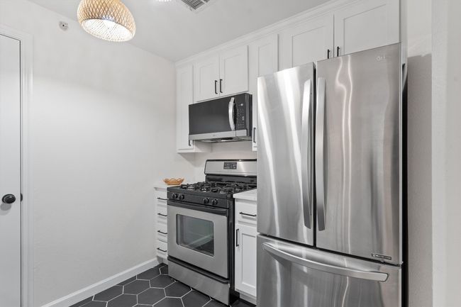 Kitchen featuring appliances with stainless steel finishes, light countertops, white cabinets, dark tile patterned floors, and baseboards | Image 9