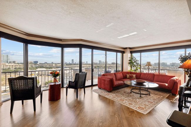 Spacious living room with large, panoramic windows offering impressive city views, sleek hardwood flooring, and a comfortable seating area. | Image 5