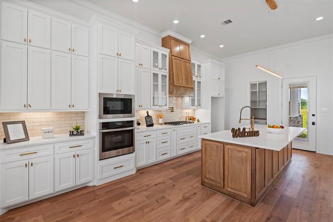 Luxurious kitchen featuring sleek white cabinetry, modern appliances, and a spacious island with elegant wood accents. Perfect for culinary creativity and entertaining. | Image 13