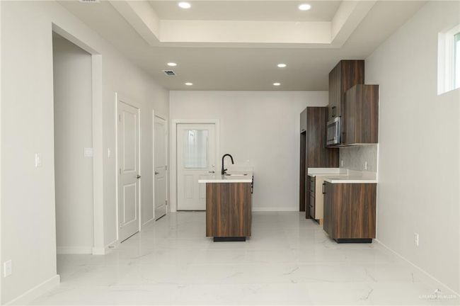 Kitchen featuring stainless steel microwave, baseboards, light countertops, recessed lighting, and a kitchen island with sink | Image 5