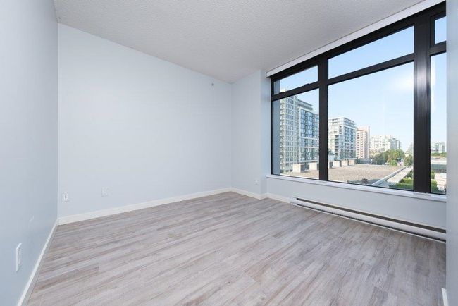 Empty room with a baseboard radiator, a textured ceiling, a view of city, and wood finished floors | Image 12
