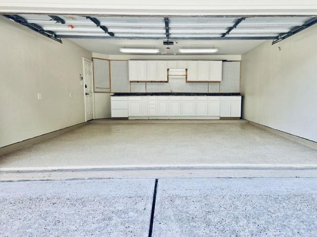 This home features a spacious, well-organized garage complete with custom cabinetry, a durable countertop workspace, and upper shelving — perfect for all your storage and project needs. | Image 34