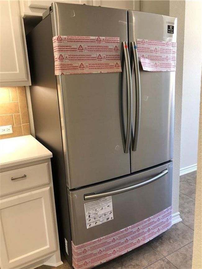 Kitchen view of freestanding refrigerator, white cabinetry, decorative backsplash, and light countertops | Image 9